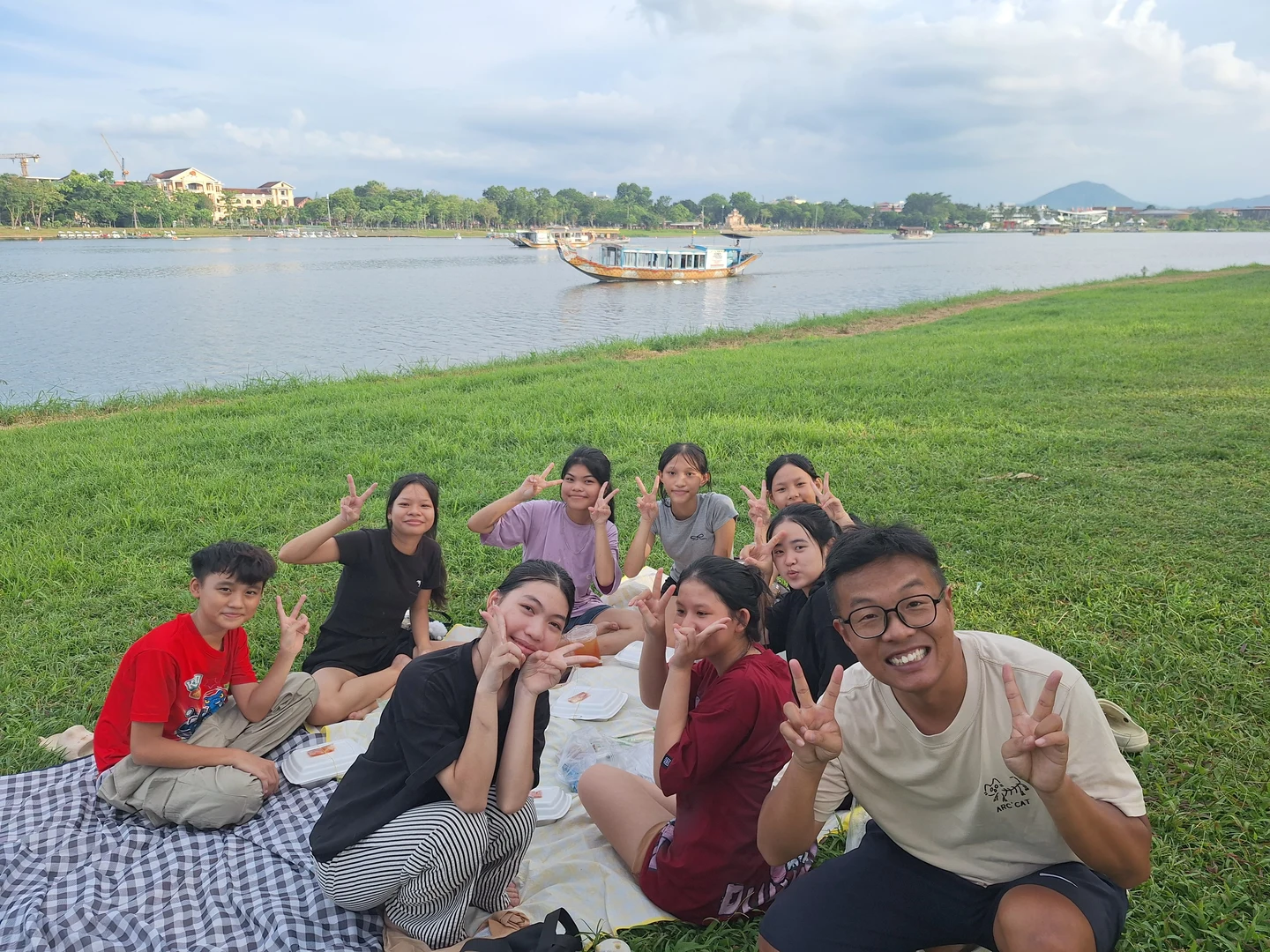 A Picnic along the Perfume River · Local teenagers gathering on the grassy riverbank for an afternoon picnic